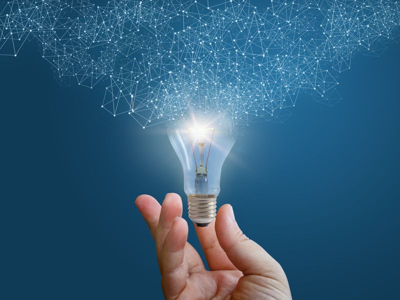 Hand holding a glowing light bulb with an abstract digital network pattern emanating from it, representing innovation and connected ideas.