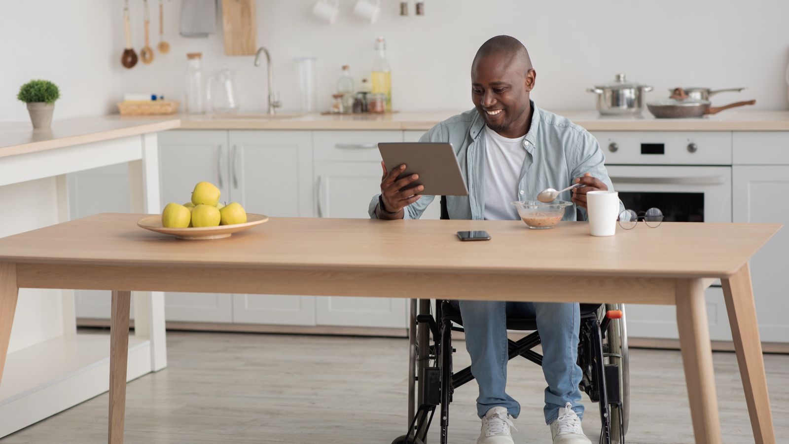 Man in a wheelchair using a tablet during breakfast in his kitchen
