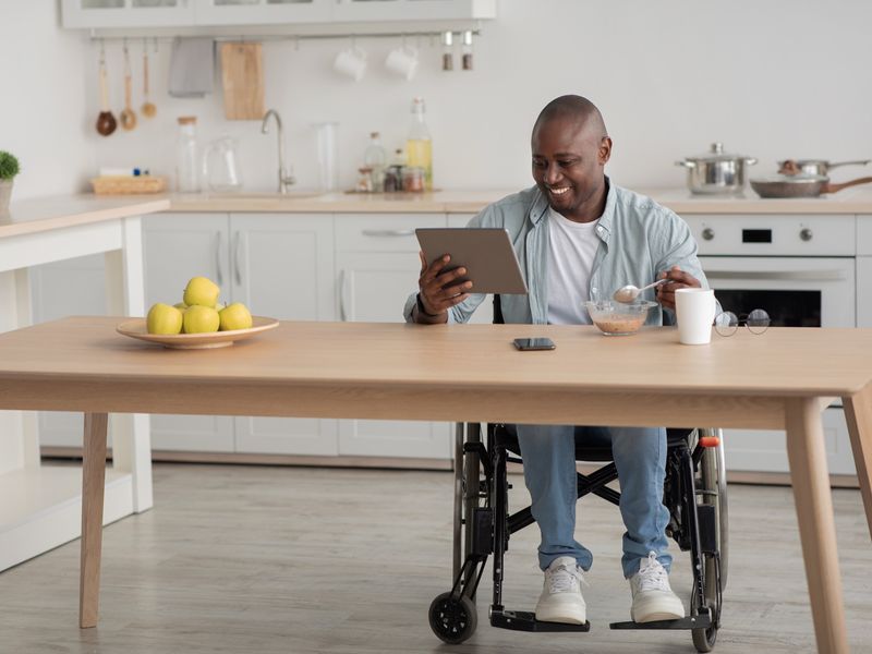 Man in a wheelchair using a tablet during breakfast in his kitchen