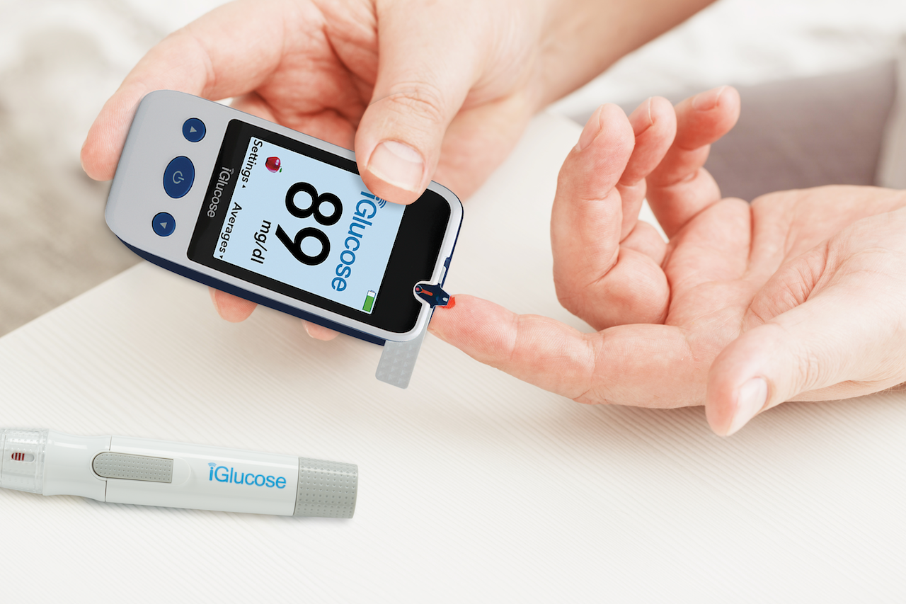 Close-up of a person using an iGlucose blood glucose meter to test blood sugar from a finger prick.