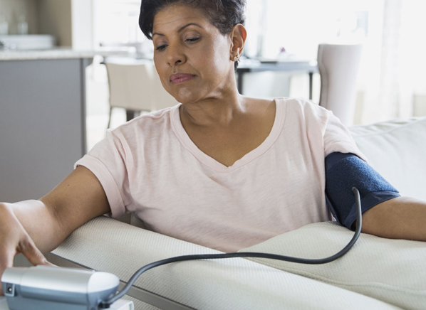 Woman at home measuring her blood pressure with an arm cuff monitor.