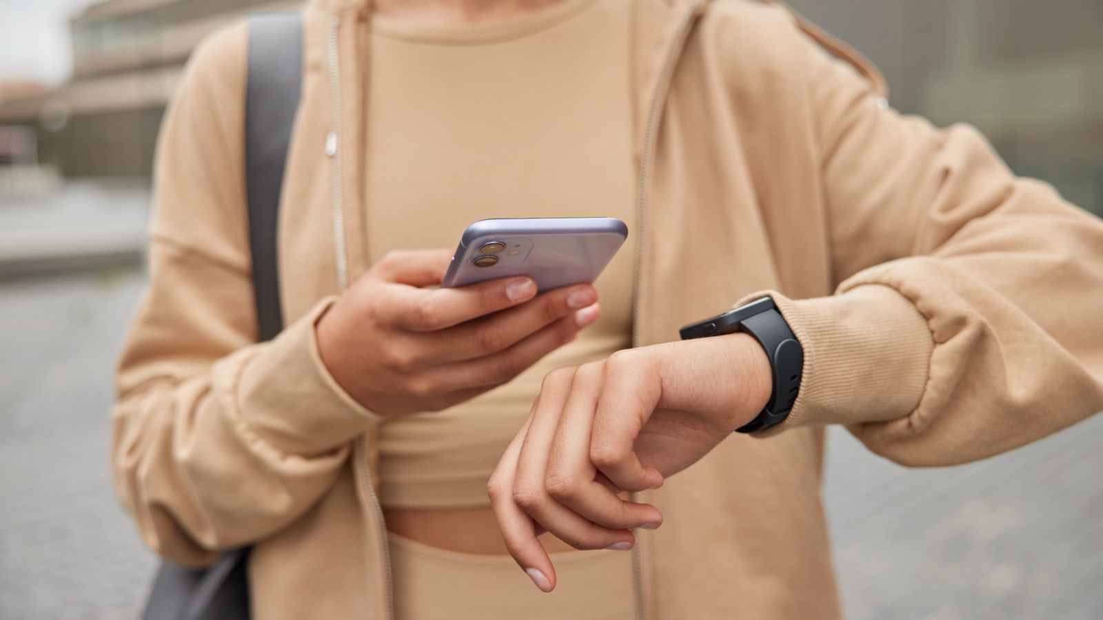 Woman in sportswear checking fitness results on her smartphone and smartwatch outdoors