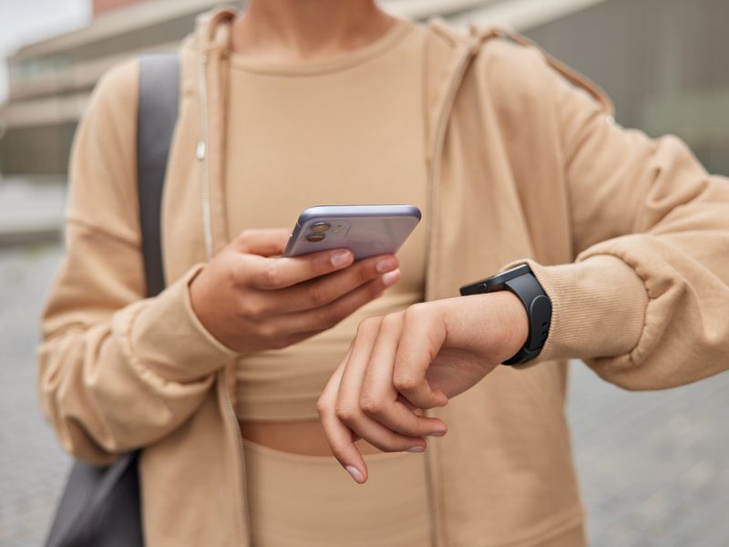 Woman in sportswear checking fitness results on her smartphone and smartwatch outdoors