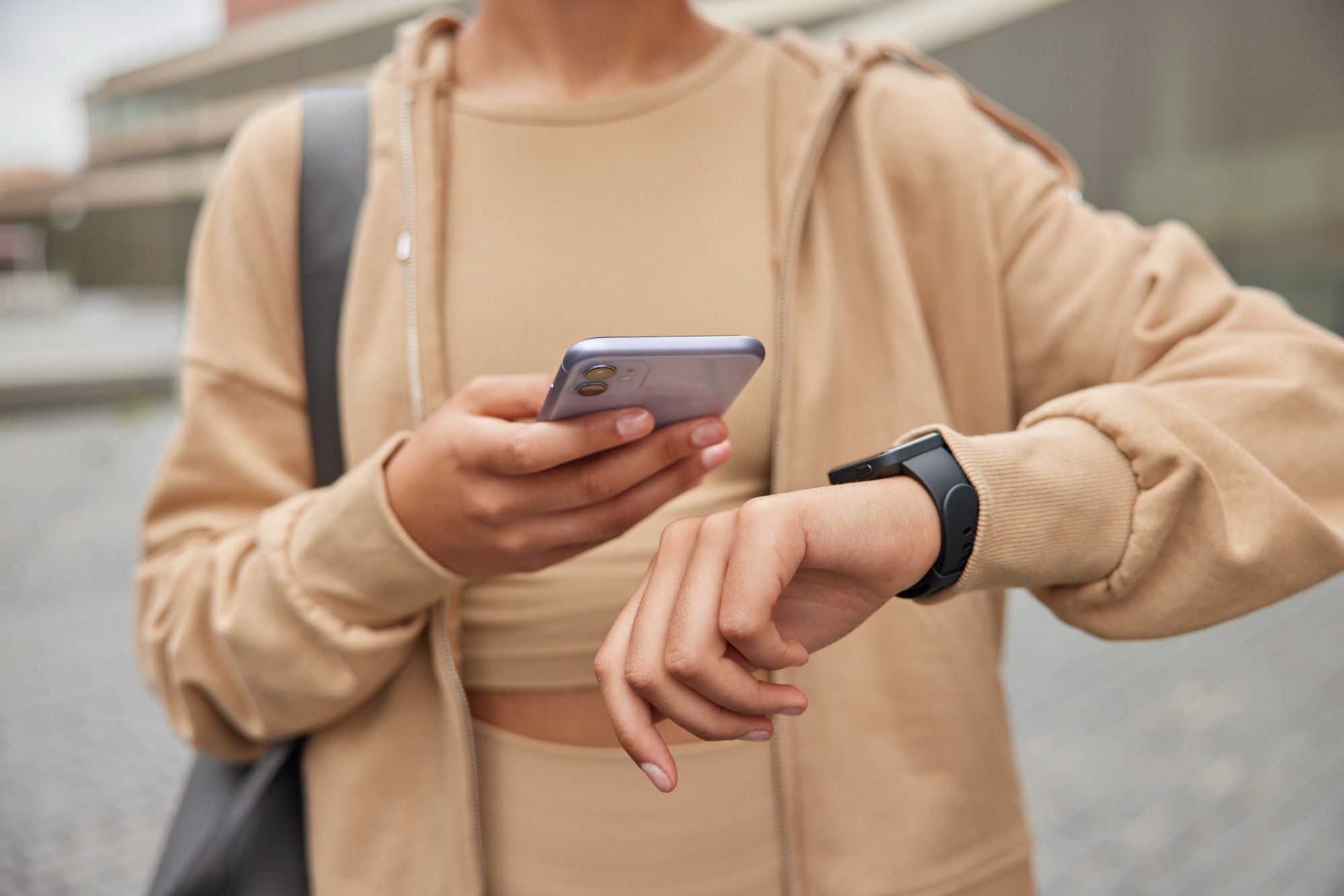 Woman in sportswear checking fitness results on her smartphone and smartwatch outdoors