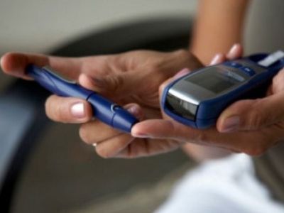 Close-up of hands holding a blood glucose meter and lancing device for diabetes testing.