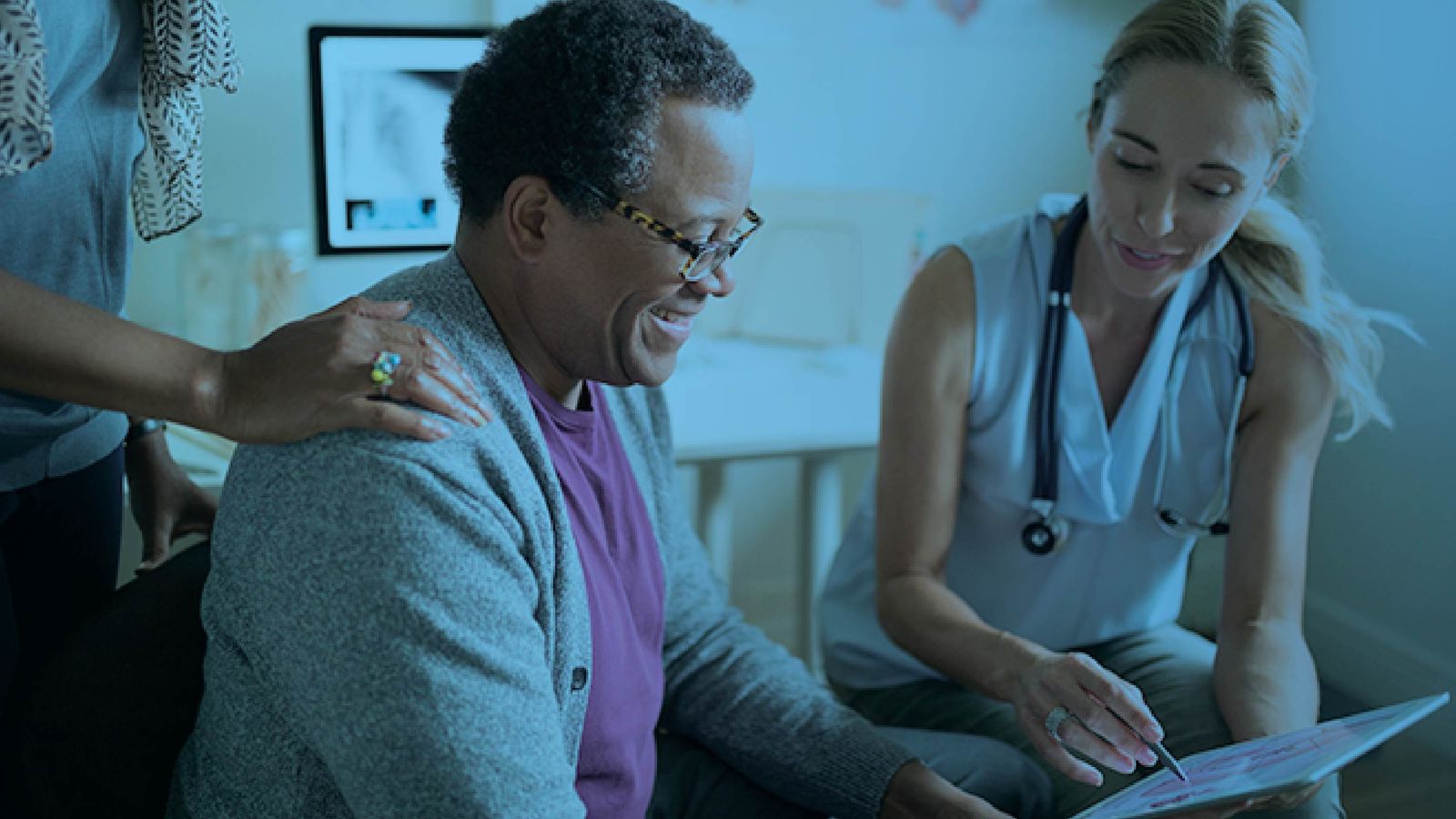Smiling elderly patient reviewing health information on a tablet with a nurse, accompanied by a family member, with a blue color overlay.