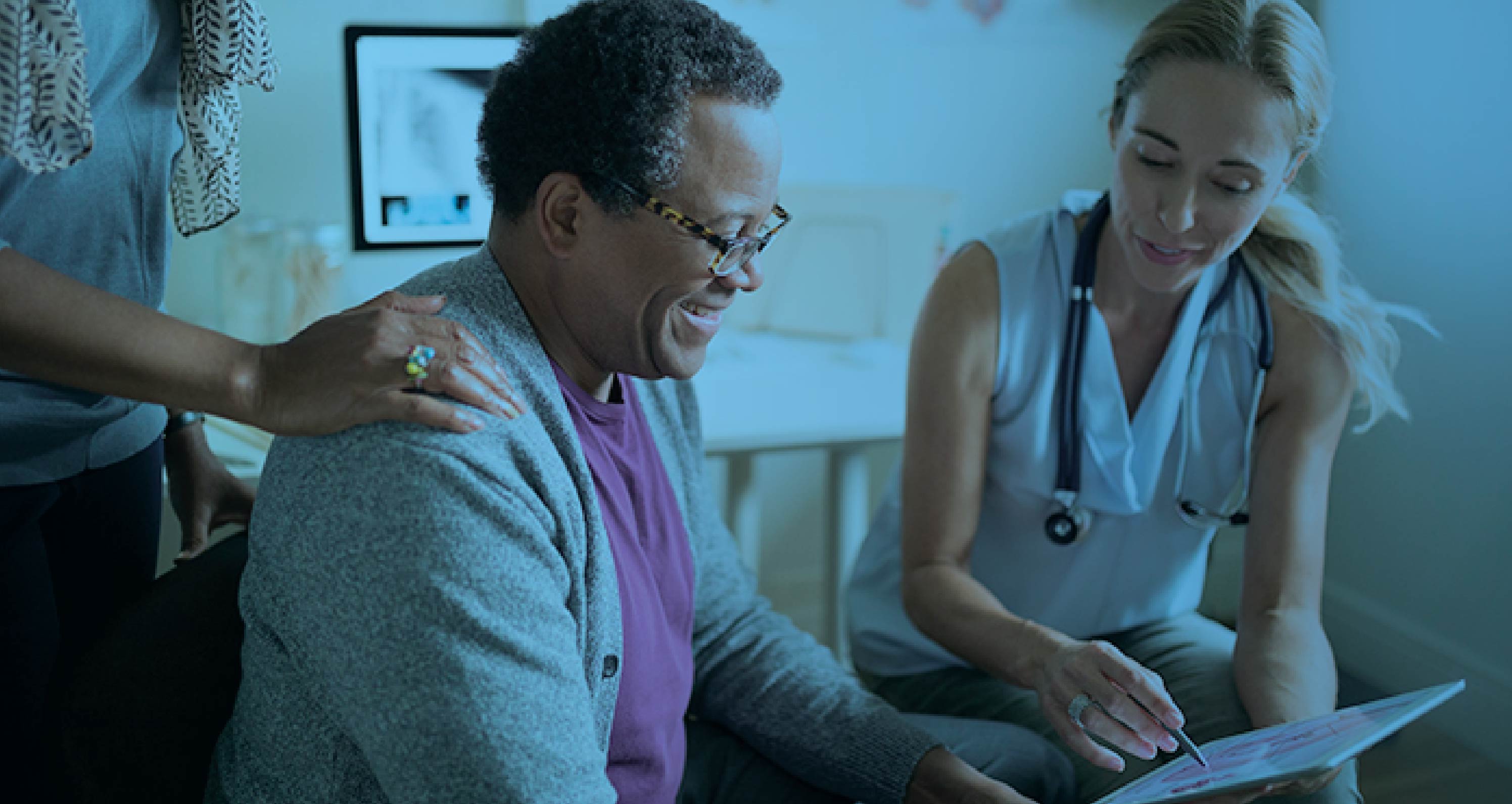 Smiling elderly patient reviewing health information on a tablet with a nurse, accompanied by a family member, with a blue color overlay.