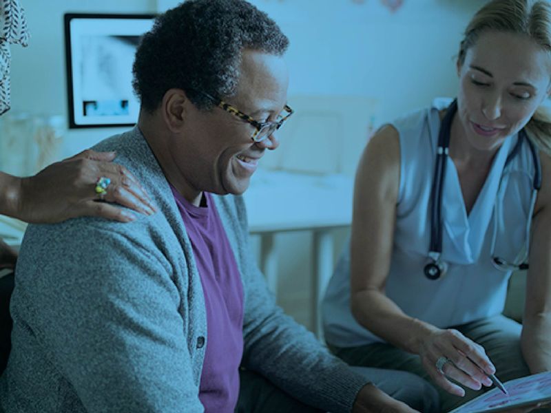 Smiling elderly patient reviewing health information on a tablet with a nurse, accompanied by a family member, with a blue color overlay.