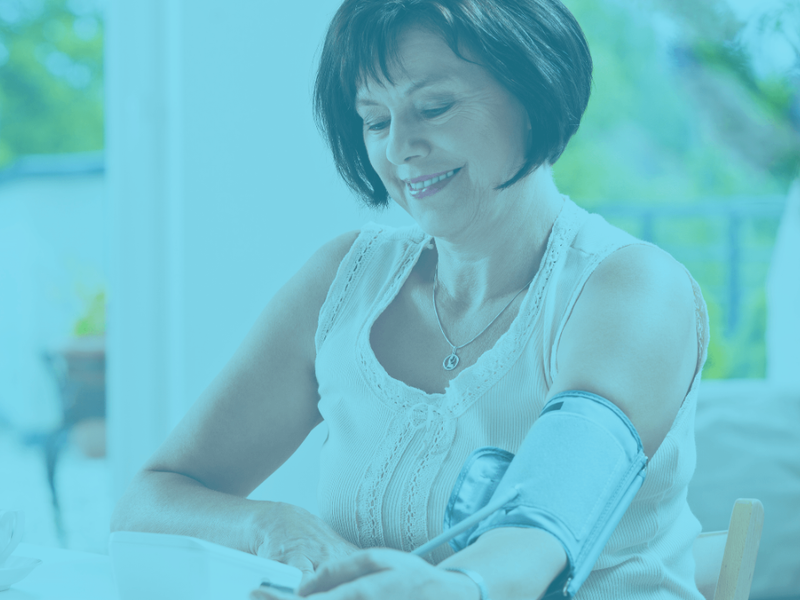 Woman using a blood pressure monitor at home, with a teal color overlay.