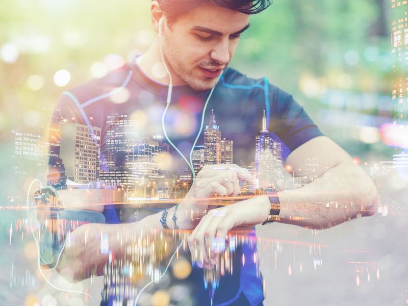 Double-exposure image of a runner checking a fitness wristwatch overlaid with a city skyline, representing connected health data