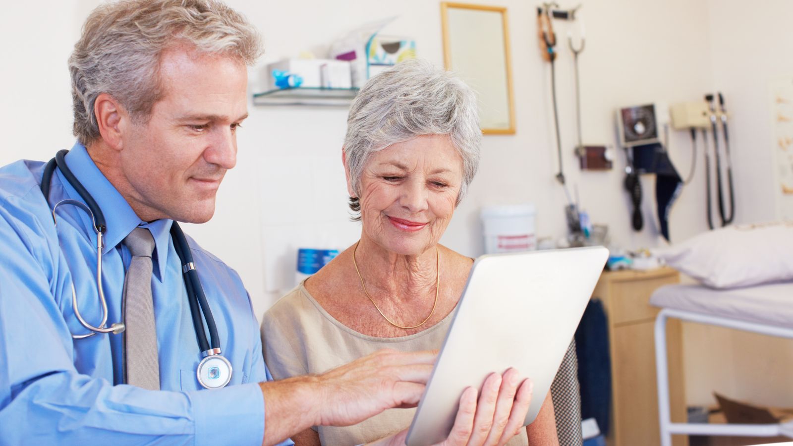 Doctor showing health information on a tablet to an elderly female patient in a clinical setting.