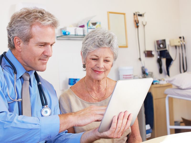Doctor showing health information on a tablet to an elderly female patient in a clinical setting.