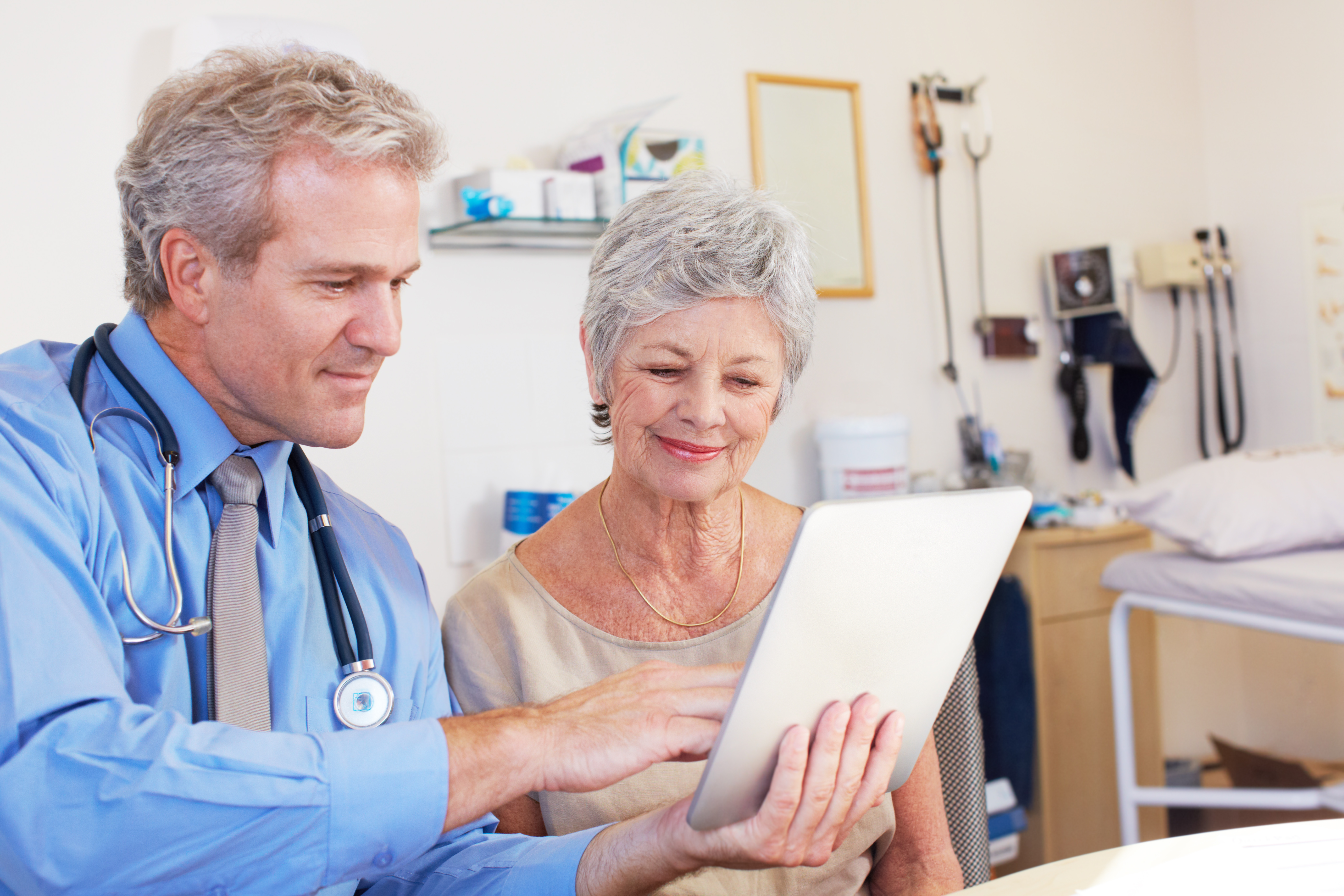 Doctor showing health information on a tablet to an elderly female patient in a clinical setting.