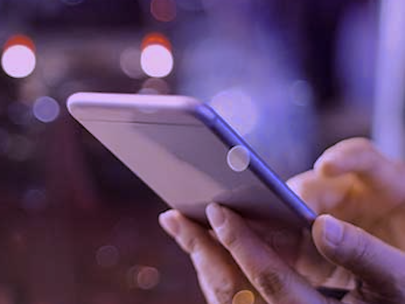 Close-up of a hand holding a smartphone with blurred city lights in the background.