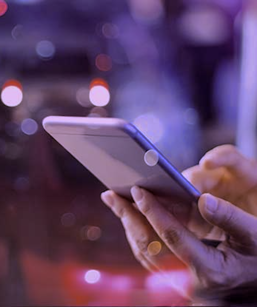 Close-up of a hand holding a smartphone with blurred city lights in the background.