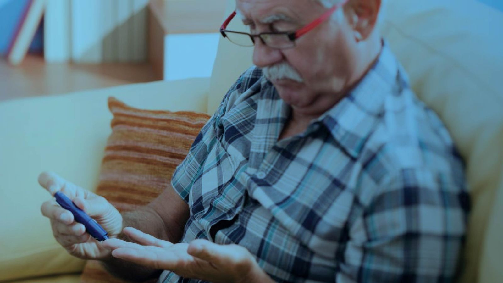 Senior man using a lancet device to test his blood sugar at home, with a blue-tinted overlay.