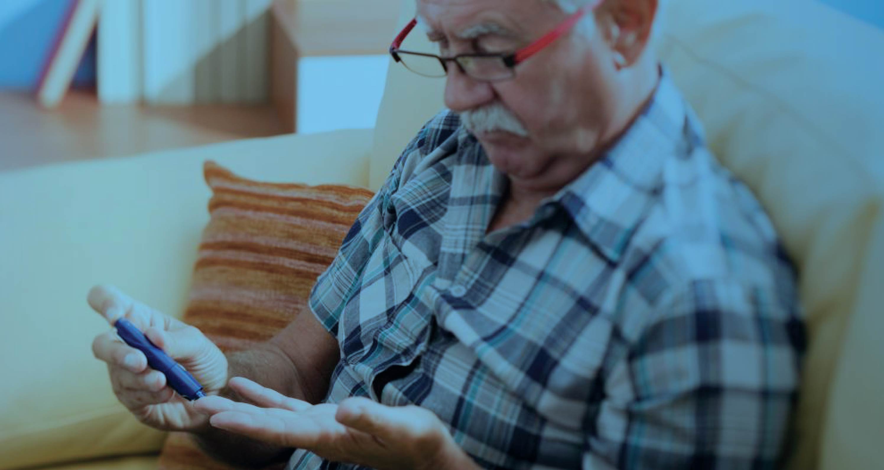 Senior man using a lancet device to test his blood sugar at home, with a blue-tinted overlay.