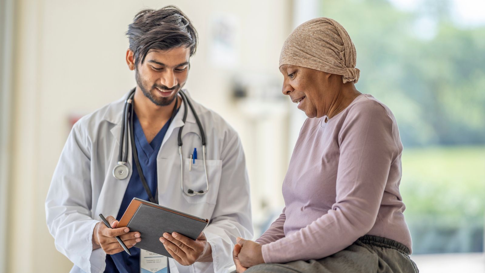 Doctor showing information on a tablet to a patient wearing a head covering during a clinical consultation.