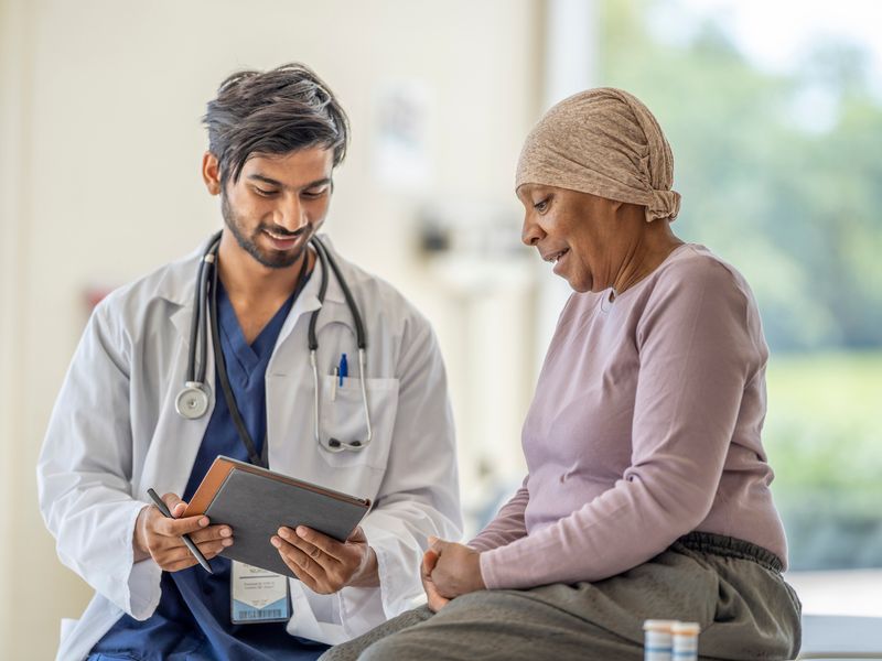 Doctor showing information on a tablet to a patient wearing a head covering during a clinical consultation.