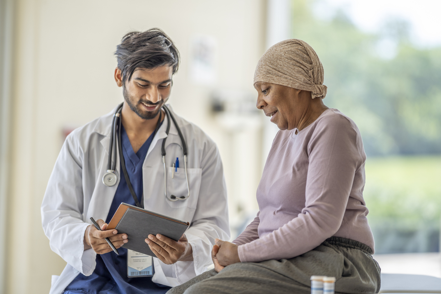 Doctor showing information on a tablet to a patient wearing a head covering during a clinical consultation.