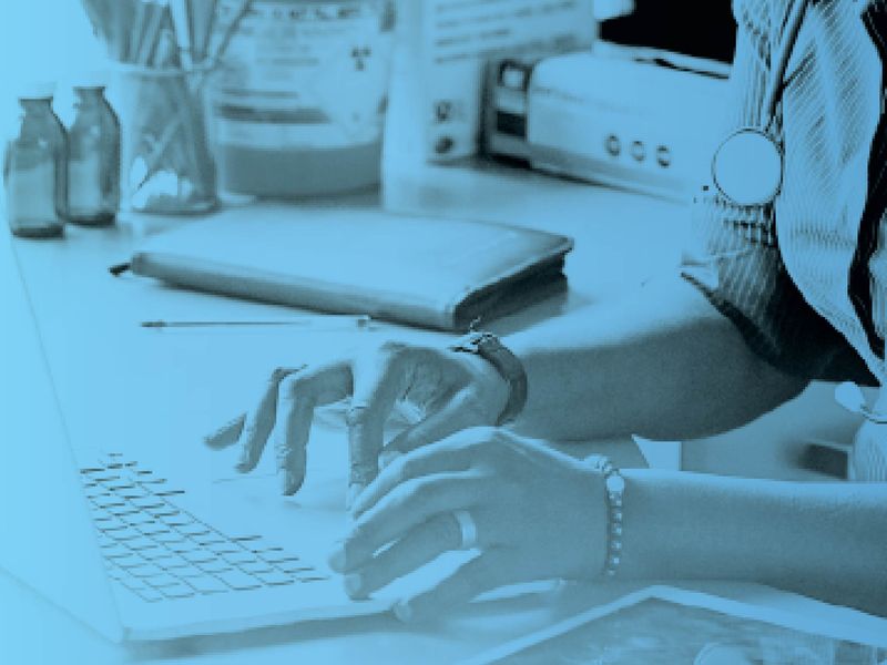 Healthcare professional with a stethoscope typing on a laptop at a desk, with a blue tint overlay.