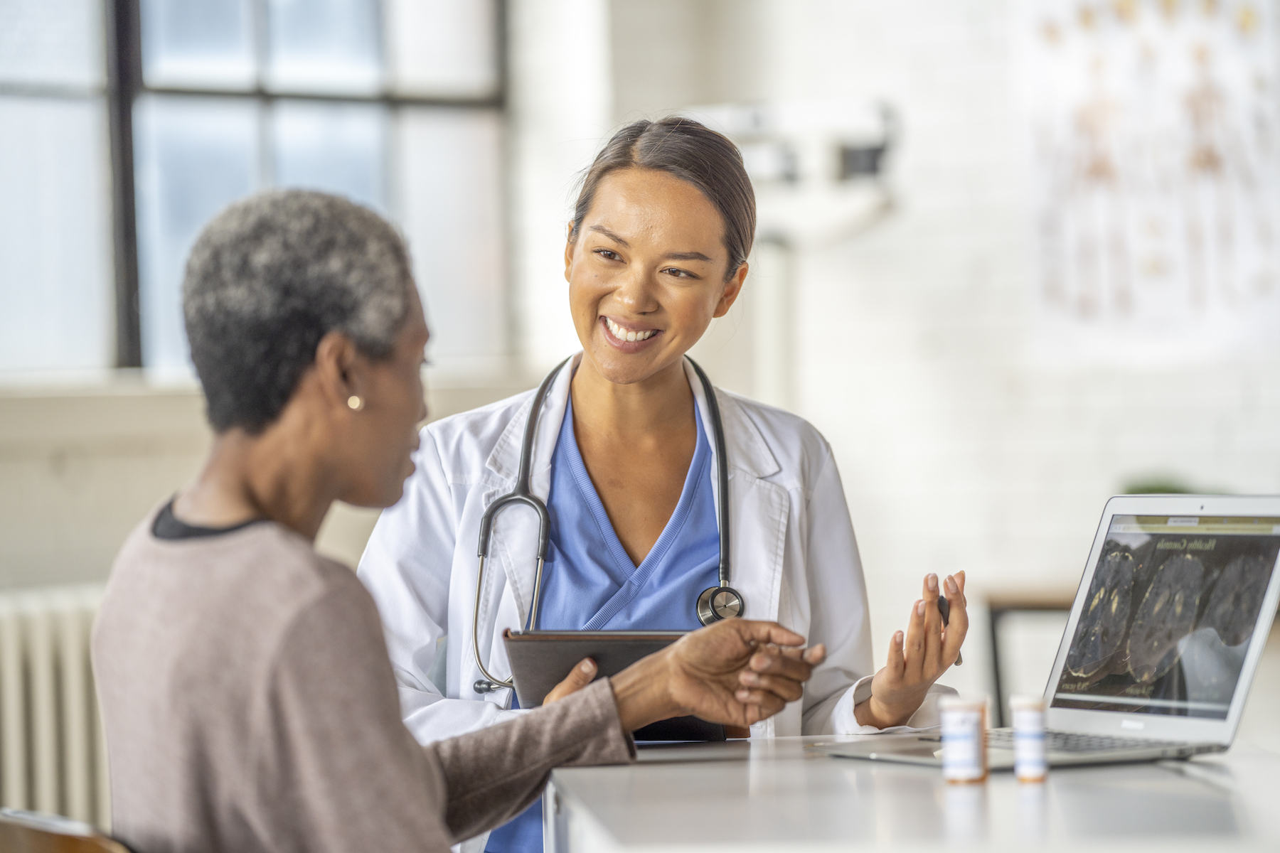 Doctor with a stethoscope smiling and discussing results on a tablet with a senior patient at an appointment.