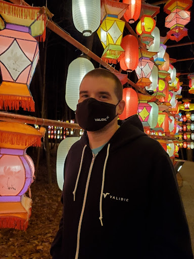 Validic employee wearing a Validic-branded hoodie and face mask standing among colorful hanging lanterns at night.