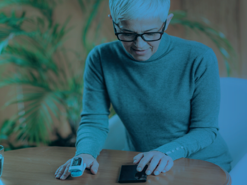Person using a pulse oximeter and smartphone to check health readings, with a blue overlay.