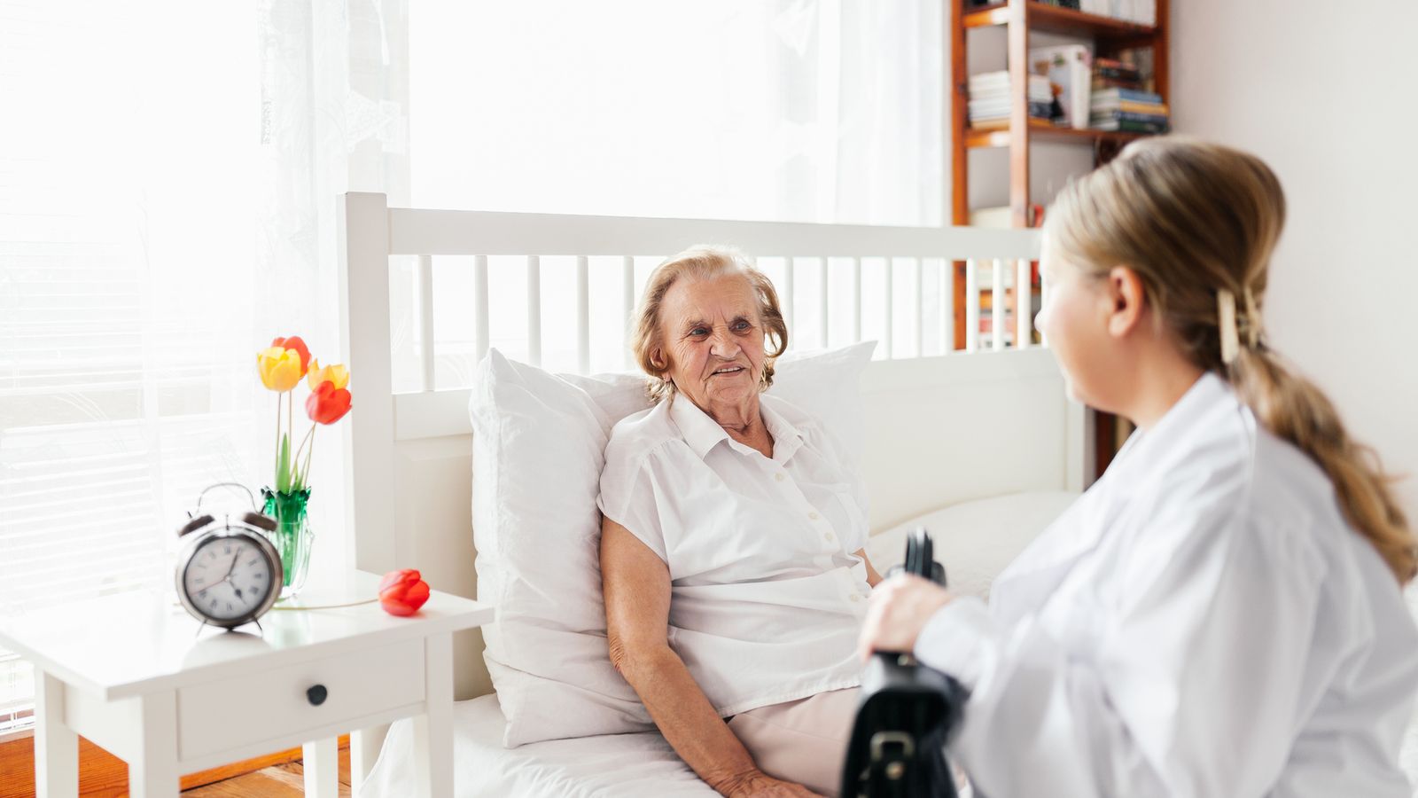 Home healthcare nurse visiting an elderly woman resting in bed.