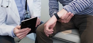 Doctor reviewing health data on a tablet while a patient wearing a fitness tracker sits nearby.