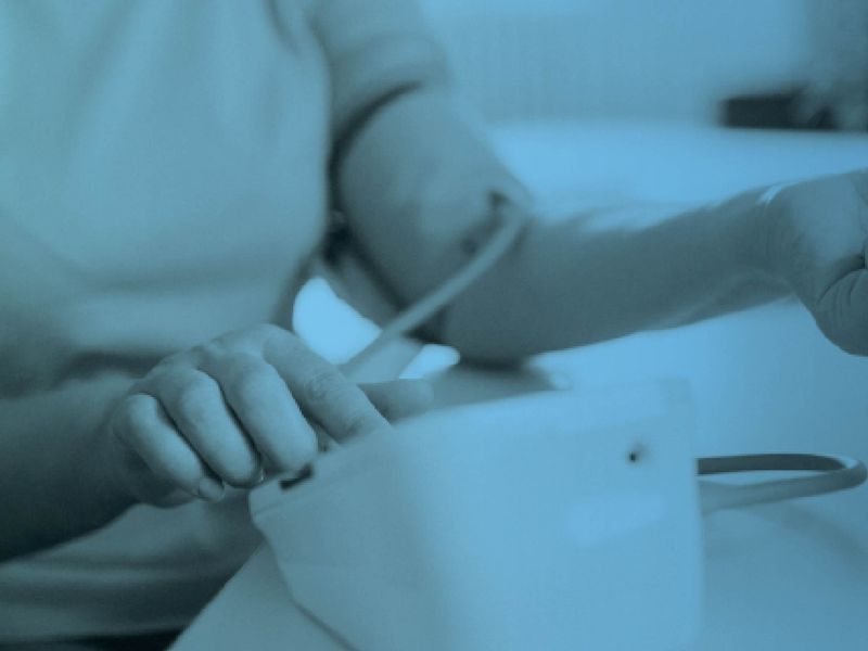 Close-up of a patient having their blood pressure taken with a cuff, shown with a blue color overlay